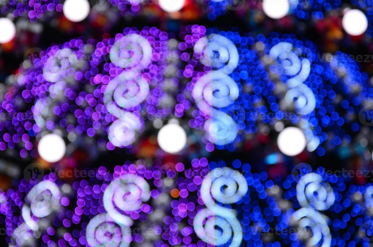 Blurred fragment of a huge Christmas tree with many luminous lamps. Defocused photo of a decorated Christmas tree close-up in bokeh technique