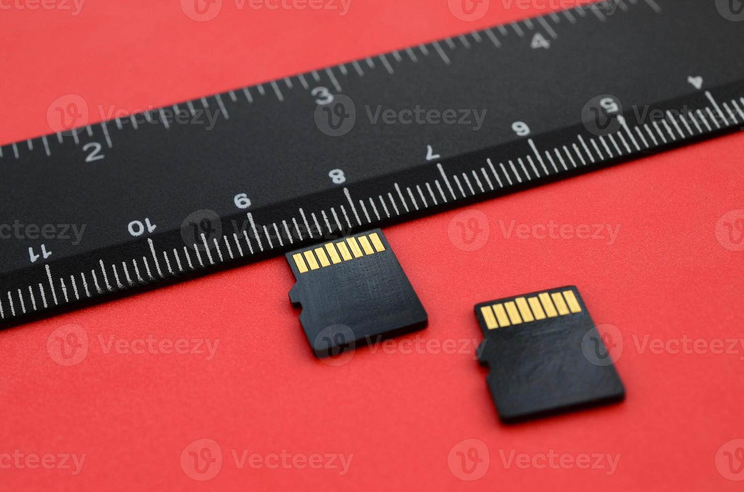 dos pequeñas tarjetas de memoria micro sd se encuentran sobre un fondo rojo junto a una regla negra. un pequeño y compacto almacén de datos e información foto