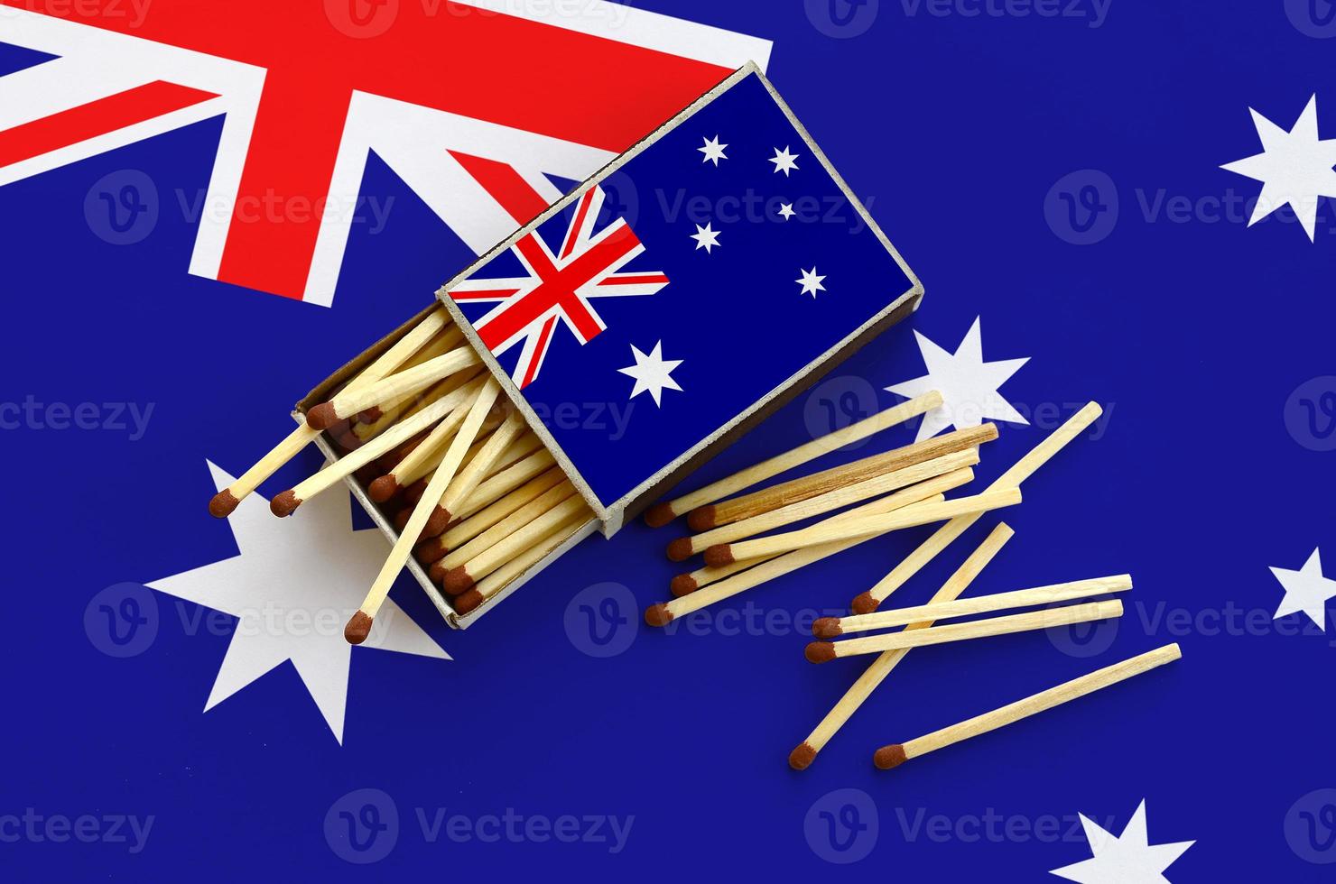 Australia flag  is shown on an open matchbox, from which several matches fall and lies on a large flag photo