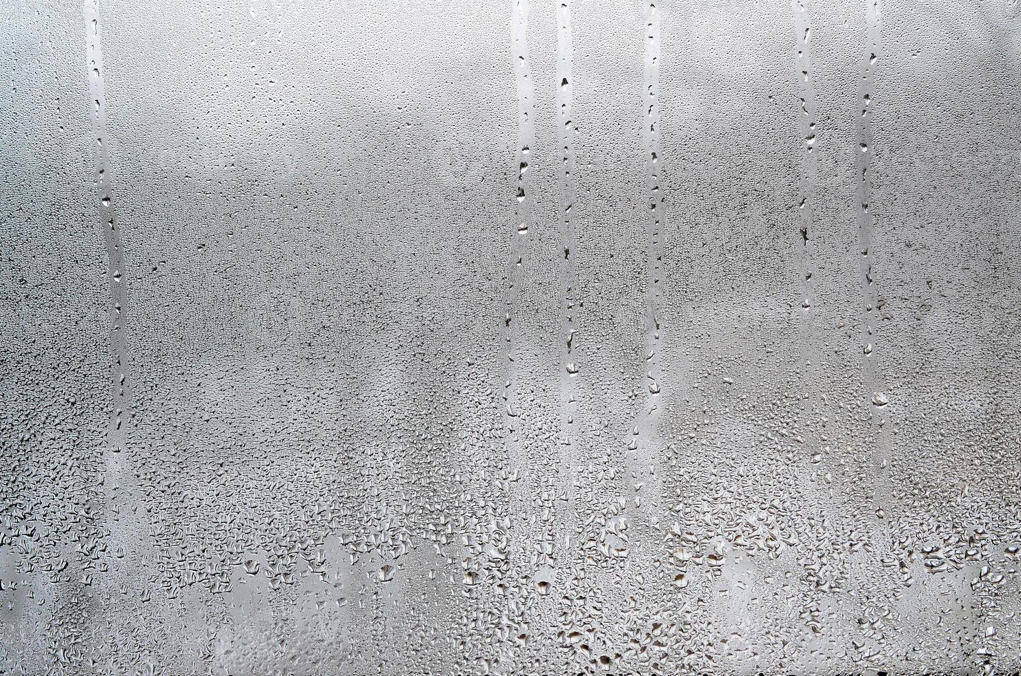 textura de una gota de lluvia sobre un fondo transparente húmedo de vidrio. tonificado en color gris foto