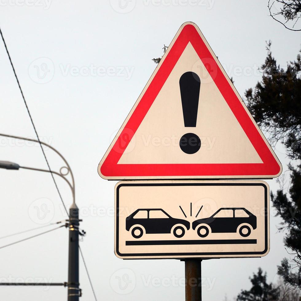 High risk of collision. A road sign with an exclamation point and two cars that crashed into each other photo