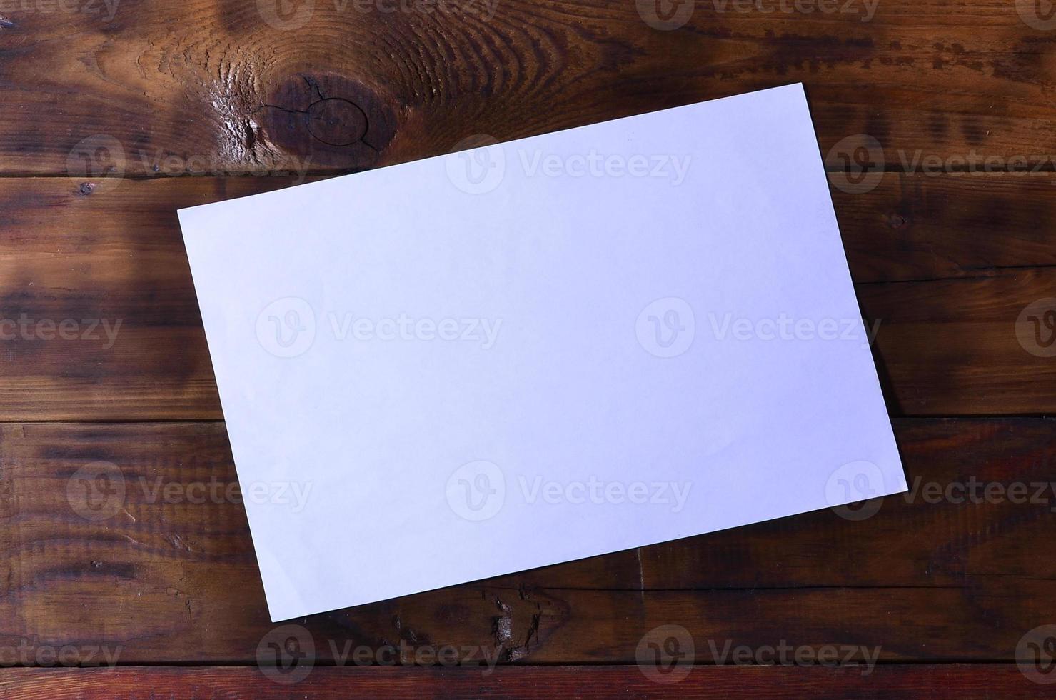 Photo of a clean white blank sheet of paper lie on a brown wooden background. Plenty of space for text