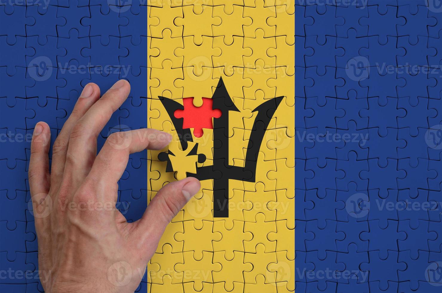 Barbados flag  is depicted on a puzzle, which the man's hand completes to fold photo