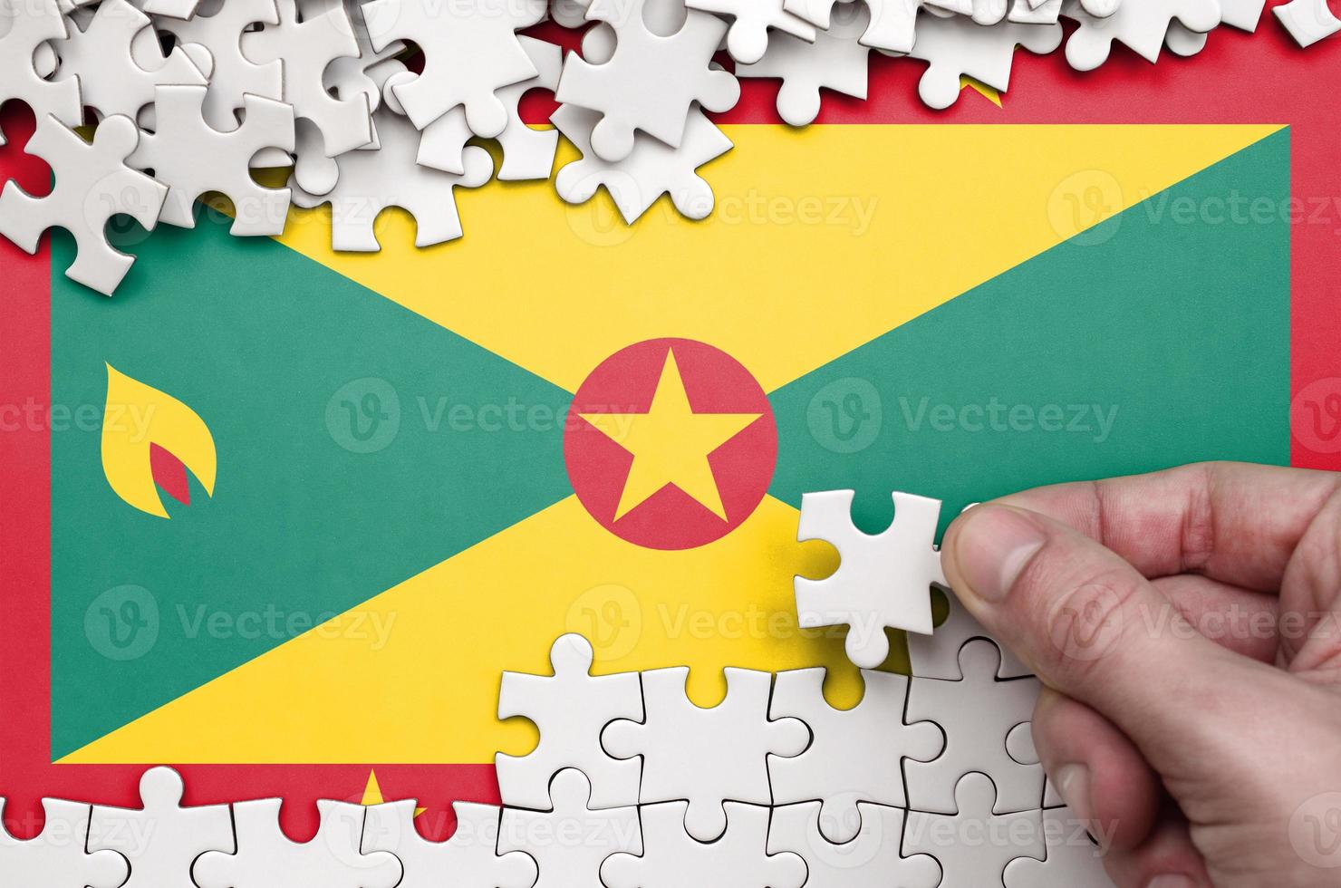 Grenada flag  is depicted on a table on which the human hand folds a puzzle of white color photo