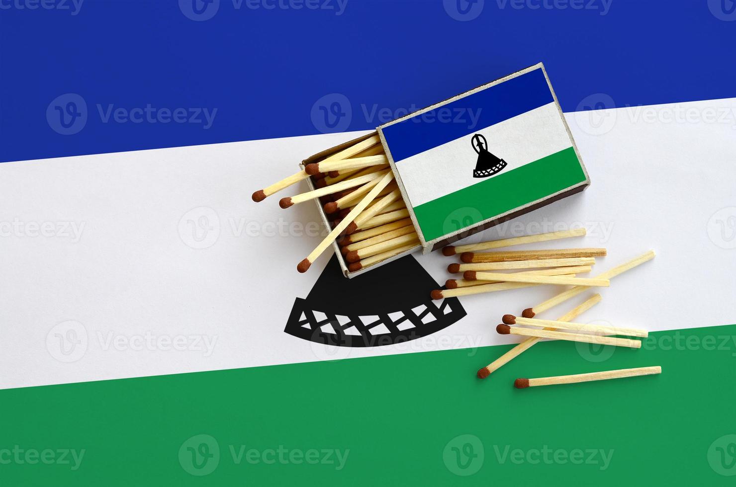 Lesotho flag  is shown on an open matchbox, from which several matches fall and lies on a large flag photo