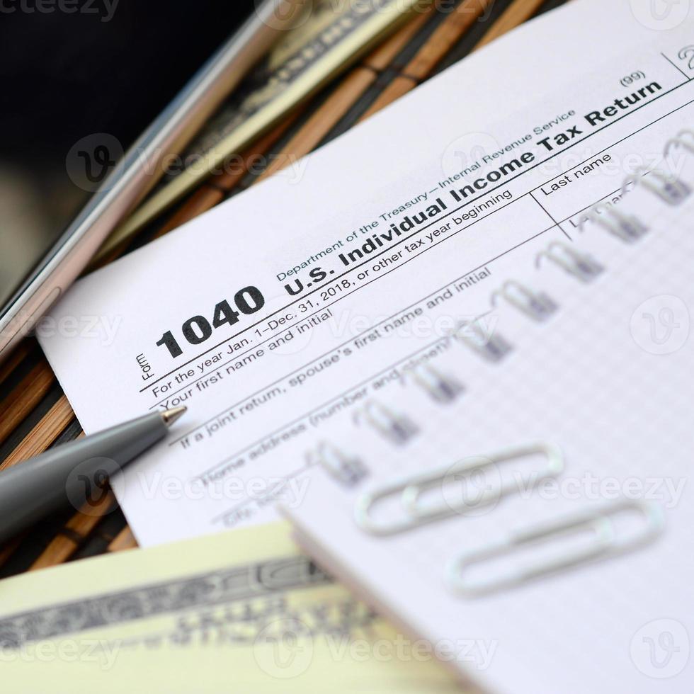 el bolígrafo, el cuaderno, el teléfono inteligente y los billetes en dólares se encuentran en el formulario de impuestos 1040 de la declaración de impuestos sobre la renta de las personas físicas. la hora de pagar impuestos foto