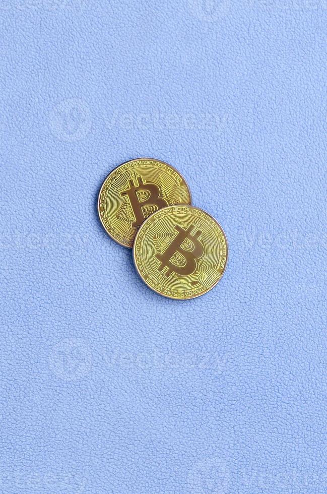 Two golden bitcoins lies on a blanket made of soft and fluffy light blue fleece fabric. Physical visualization of virtual crypto currency photo