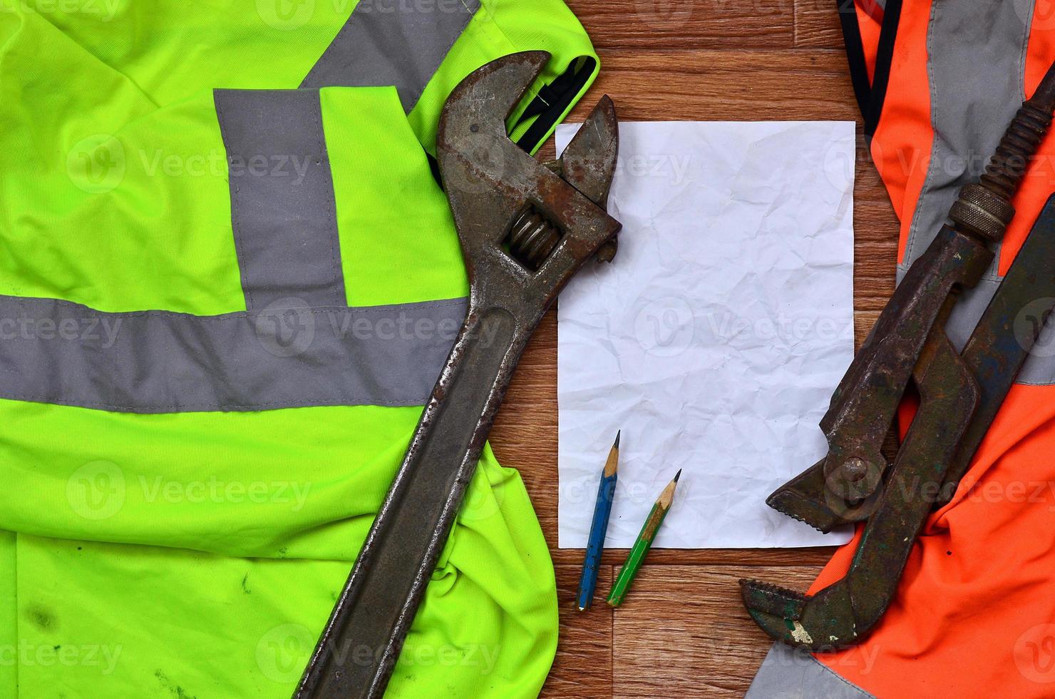 A crumpled sheet of paper with two pencils surrounded by green and orange working uniforms and adjustable wrenches photo