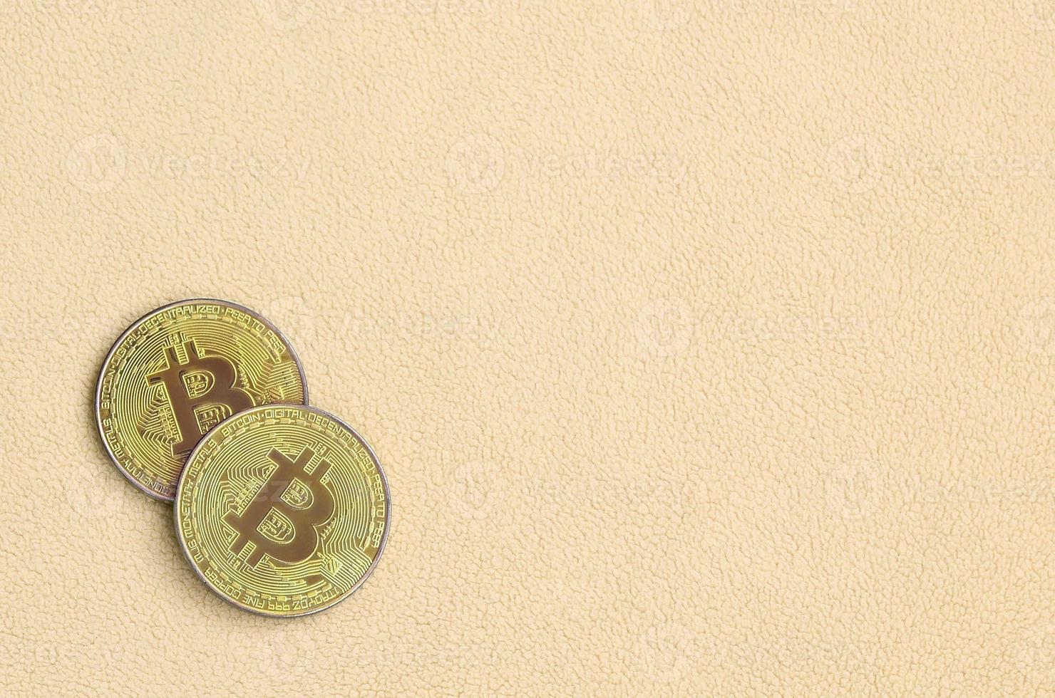 Two golden bitcoins lies on a blanket made of soft and fluffy light orange fleece fabric. Physical visualization of virtual crypto currency photo