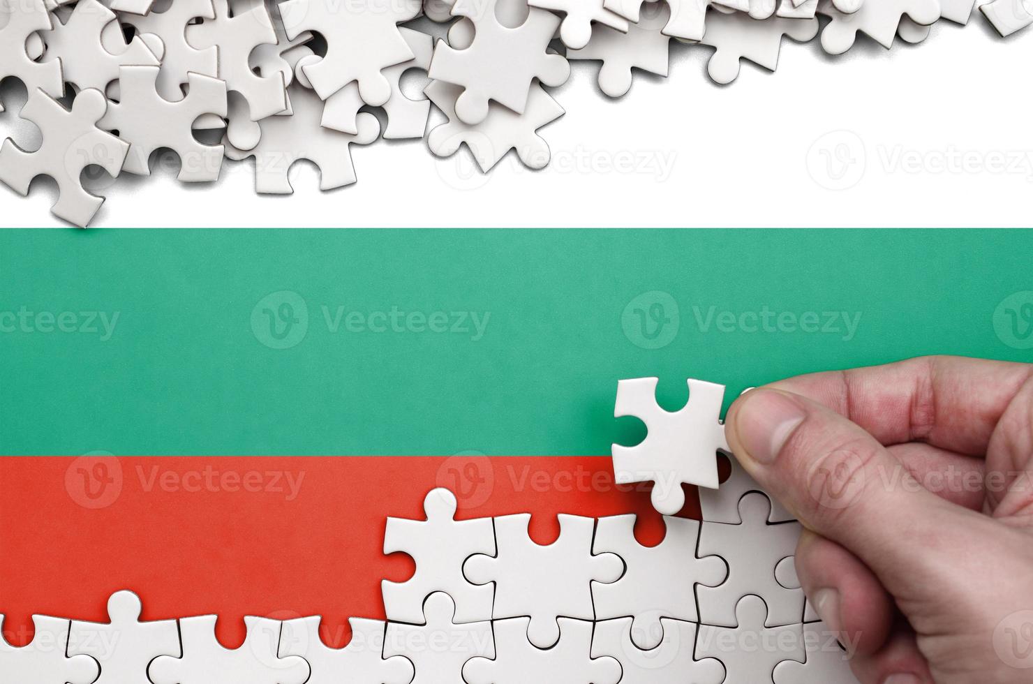 Bulgaria flag  is depicted on a table on which the human hand folds a puzzle of white color photo