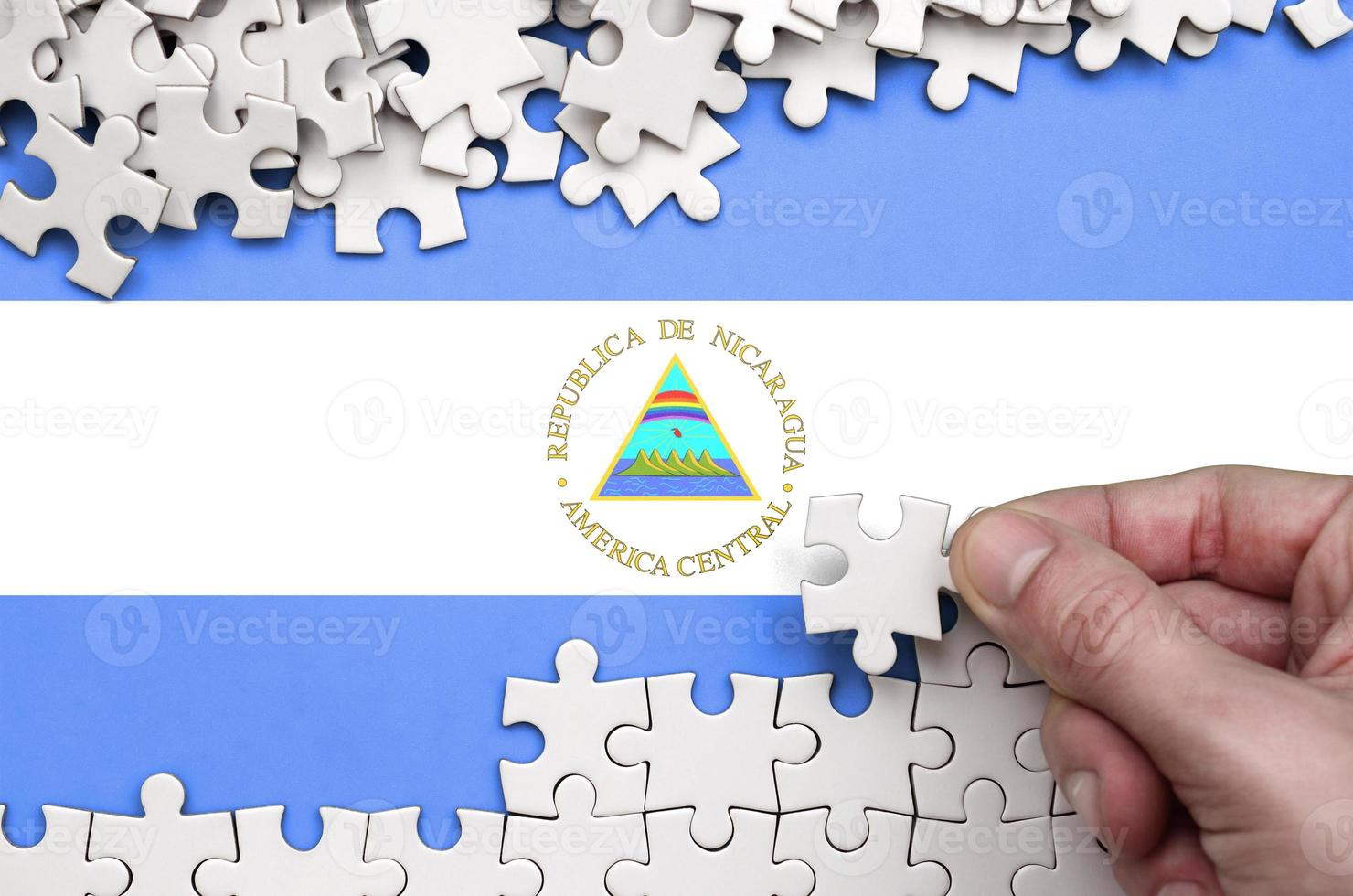 Nicaragua flag  is depicted on a table on which the human hand folds a puzzle of white color photo