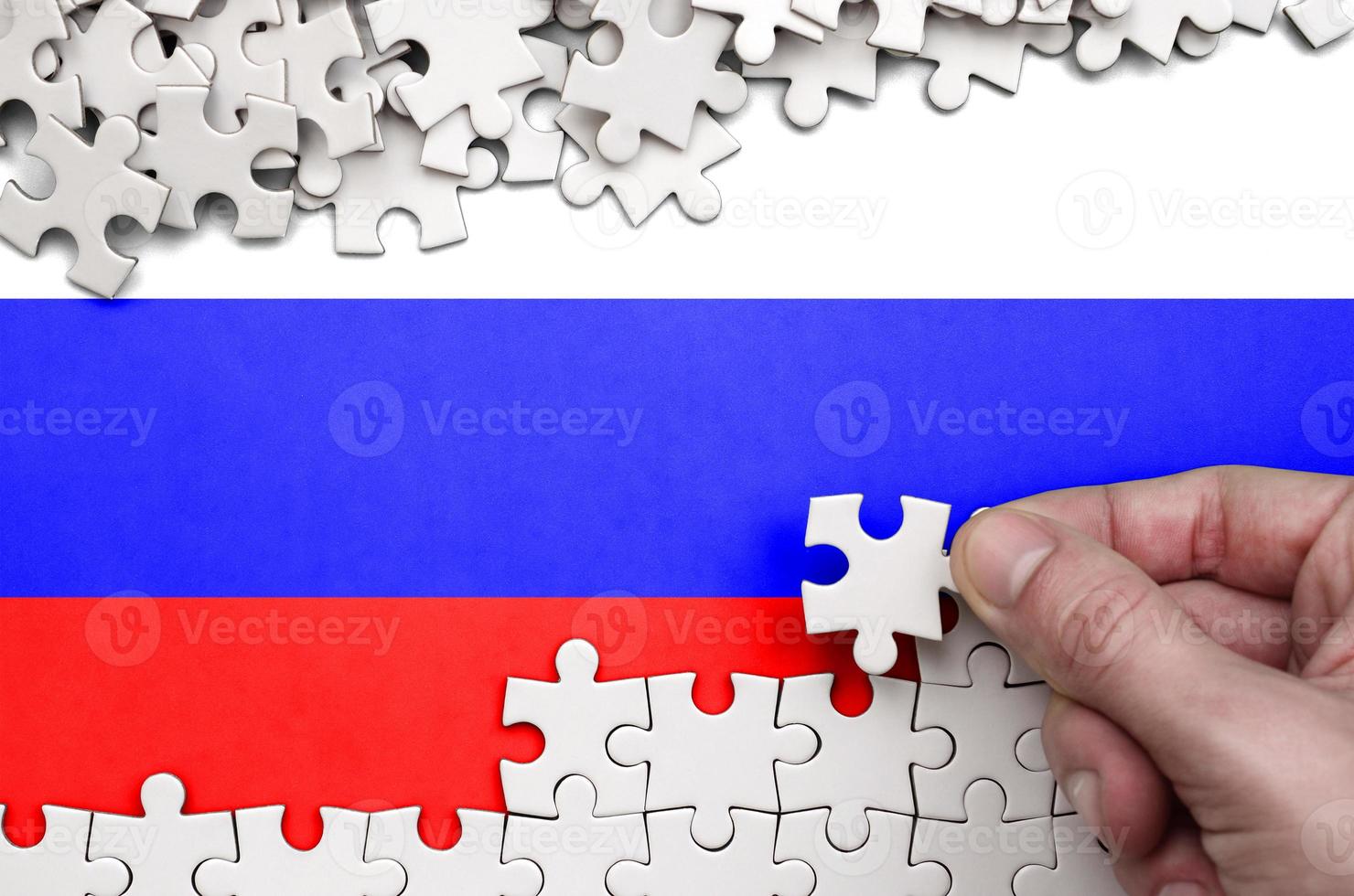 Russia flag  is depicted on a table on which the human hand folds a puzzle of white color photo