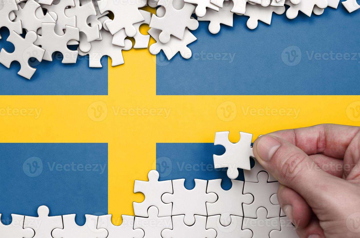 Sweden flag  is depicted on a table on which the human hand folds a puzzle of white color photo