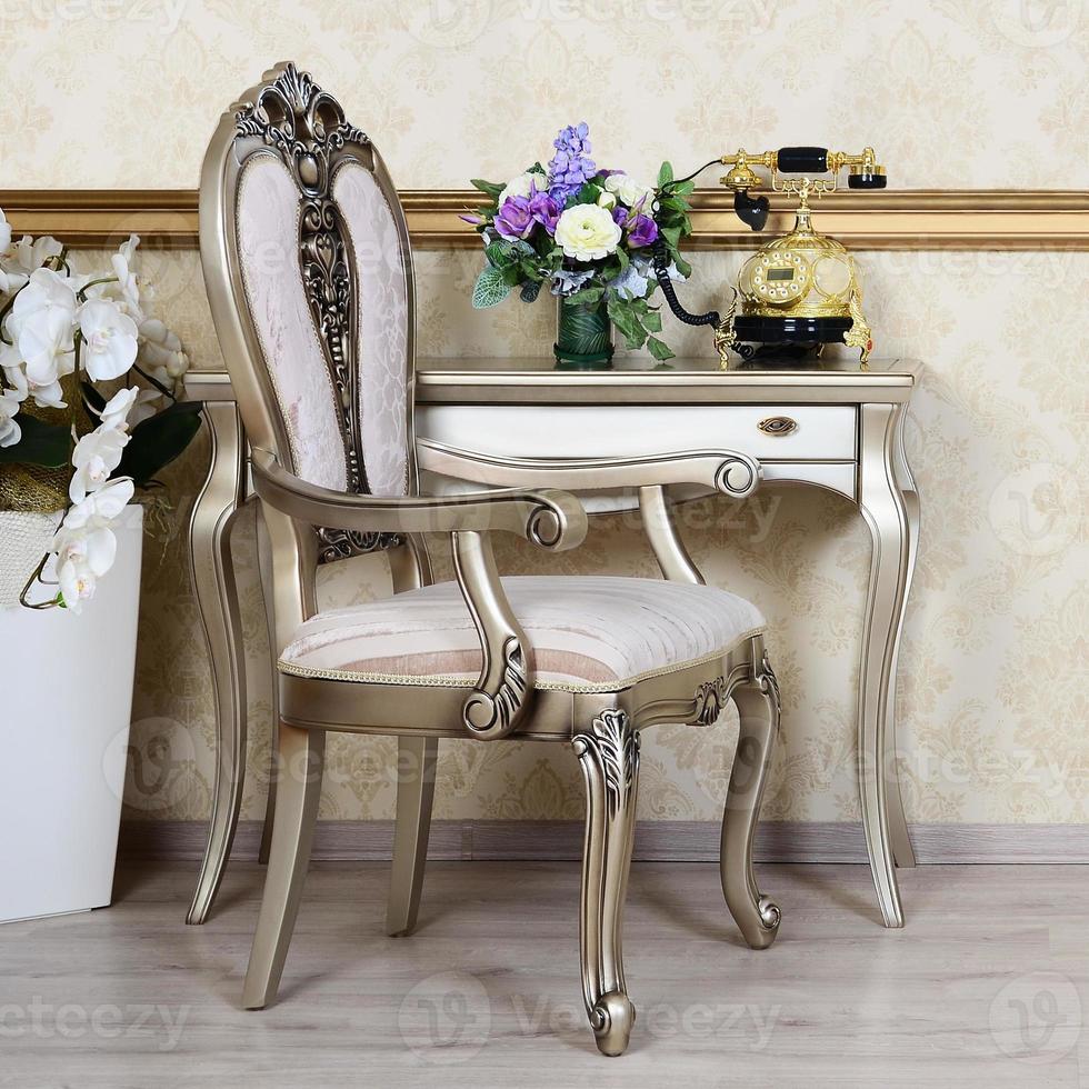 A fragment of a retro interior with a chair and a desk on which is located a telephone and a vase of flowers photo