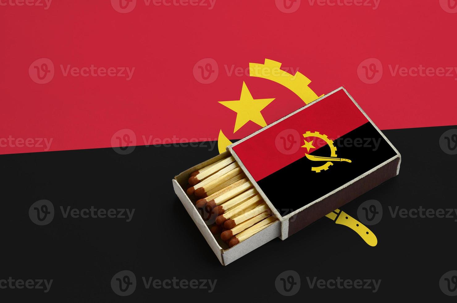 Angola flag  is shown in an open matchbox, which is filled with matches and lies on a large flag photo