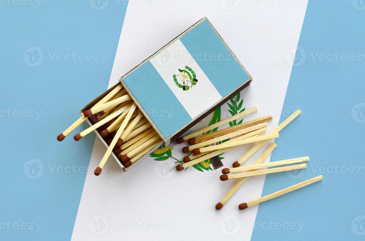 Guatemala flag  is shown on an open matchbox, from which several matches fall and lies on a large flag photo
