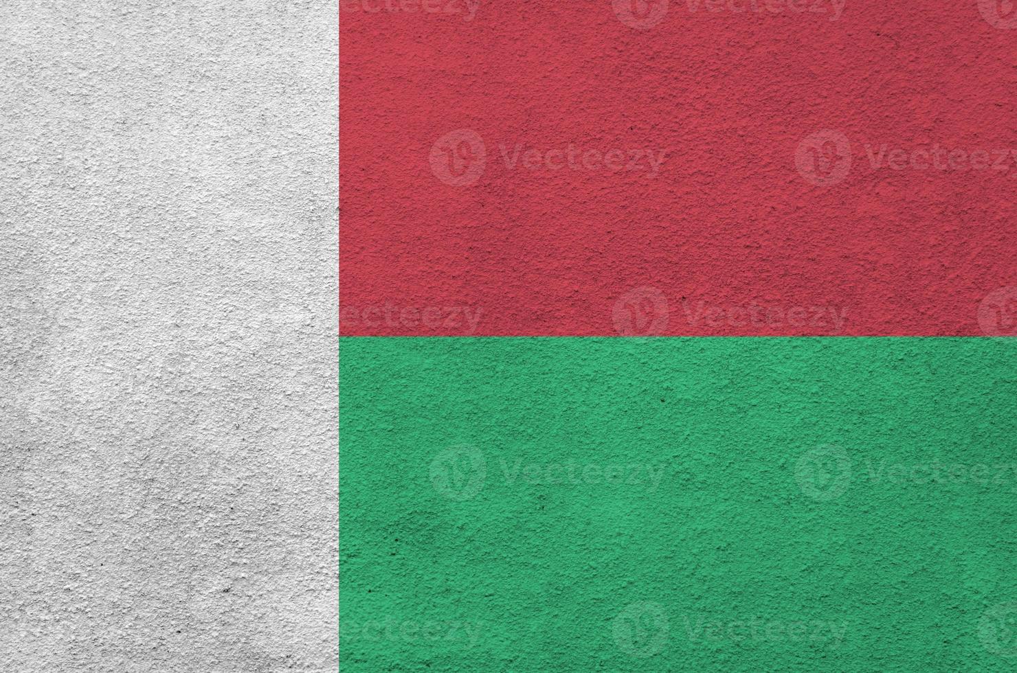 Madagascar flag depicted in bright paint colors on old relief plastering wall. Textured banner on rough background photo