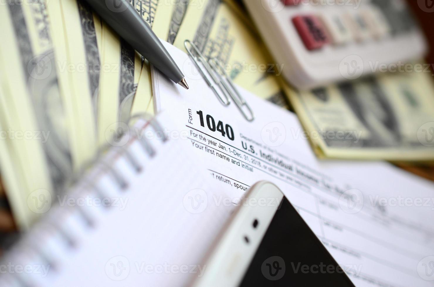 el bolígrafo, el cuaderno, la calculadora, el teléfono inteligente y los billetes en dólares se encuentran en el formulario de impuestos 1040 declaración de impuestos sobre la renta individual de EE. UU. la hora de pagar impuestos foto