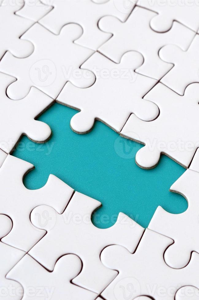 Close-up texture of a white jigsaw puzzle in assembled state with missing elements forming a blue pad for text. Copy space photo