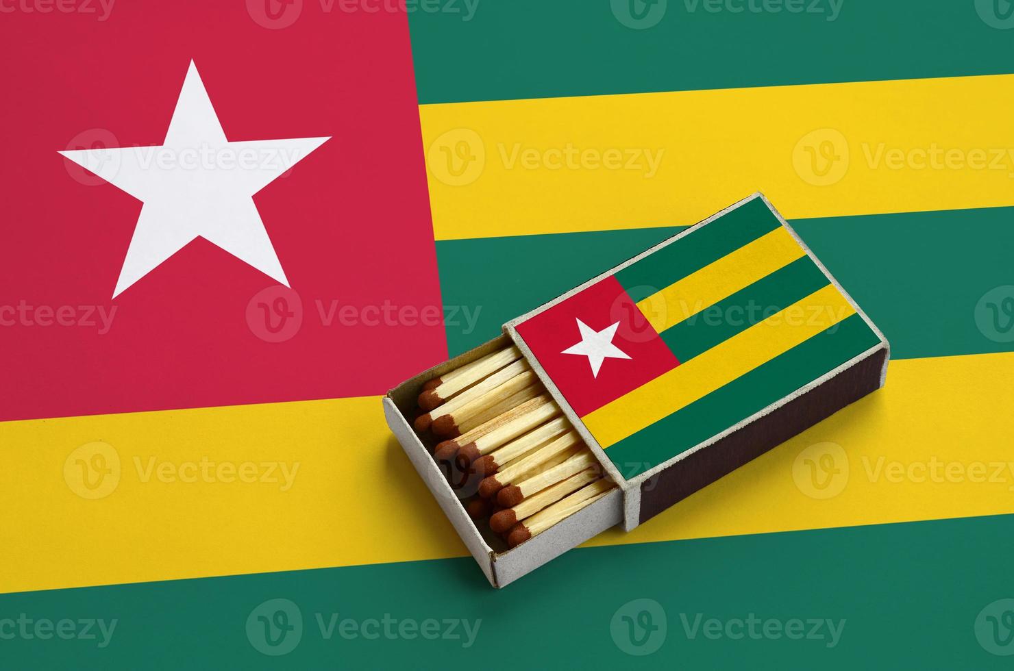 Togo flag  is shown in an open matchbox, which is filled with matches and lies on a large flag photo