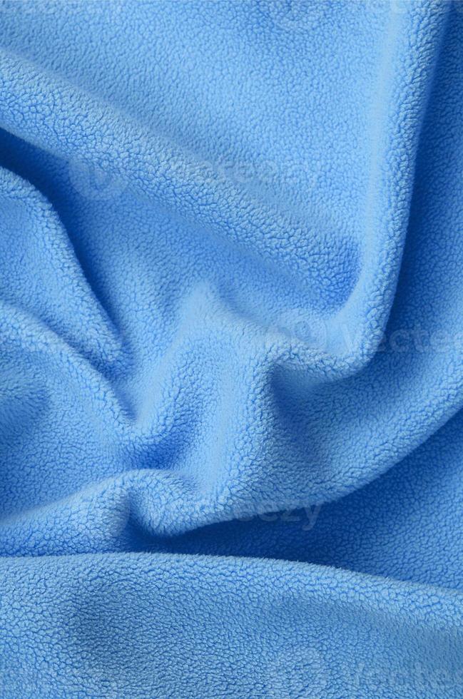 The blanket of furry blue fleece fabric. A background of light blue soft plush fleece material with a lot of relief folds photo