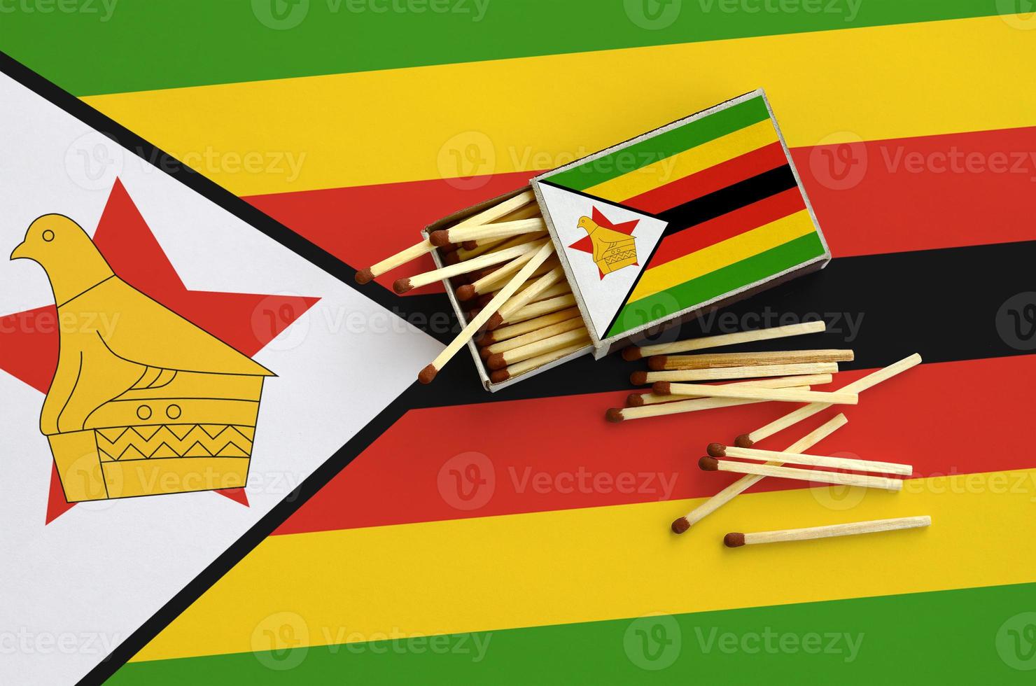Zimbabwe flag  is shown on an open matchbox, from which several matches fall and lies on a large flag photo