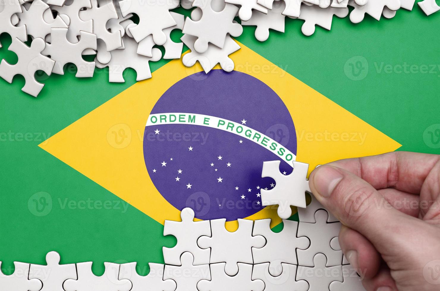 la bandera de brasil está representada en una mesa en la que la mano humana dobla un rompecabezas de color blanco foto