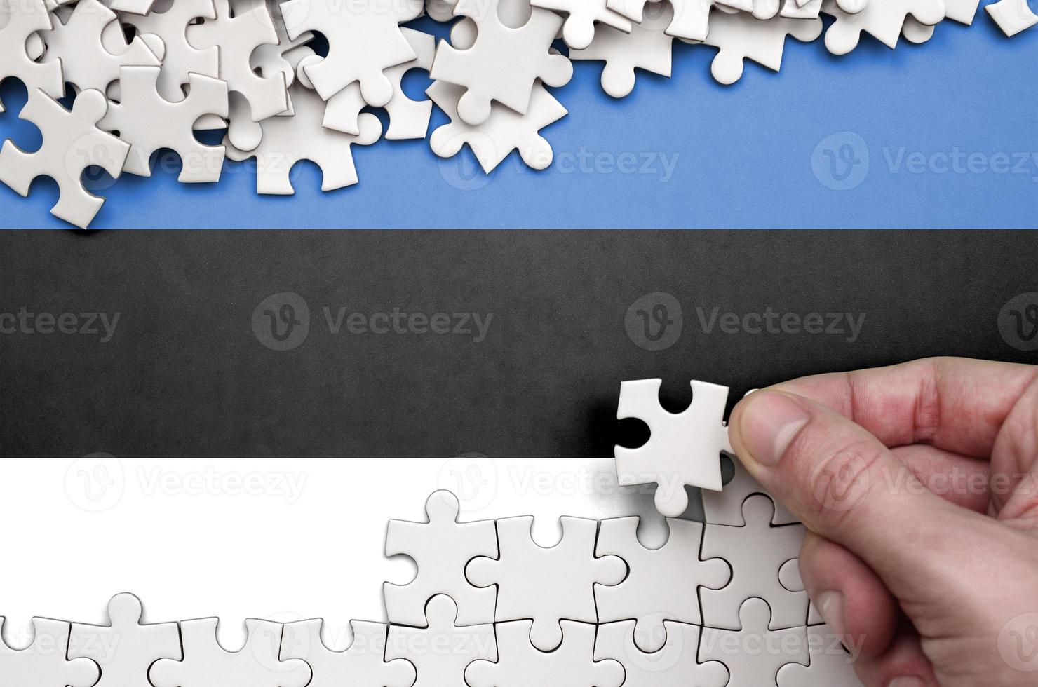 Estonia flag  is depicted on a table on which the human hand folds a puzzle of white color photo