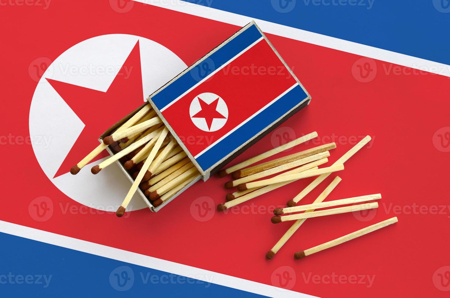 North Korea flag  is shown on an open matchbox, from which several matches fall and lies on a large flag photo