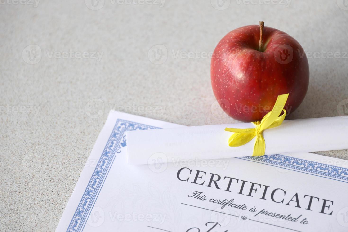 A certificate of achievement lies on table with small scroll and red apple. Education documents photo