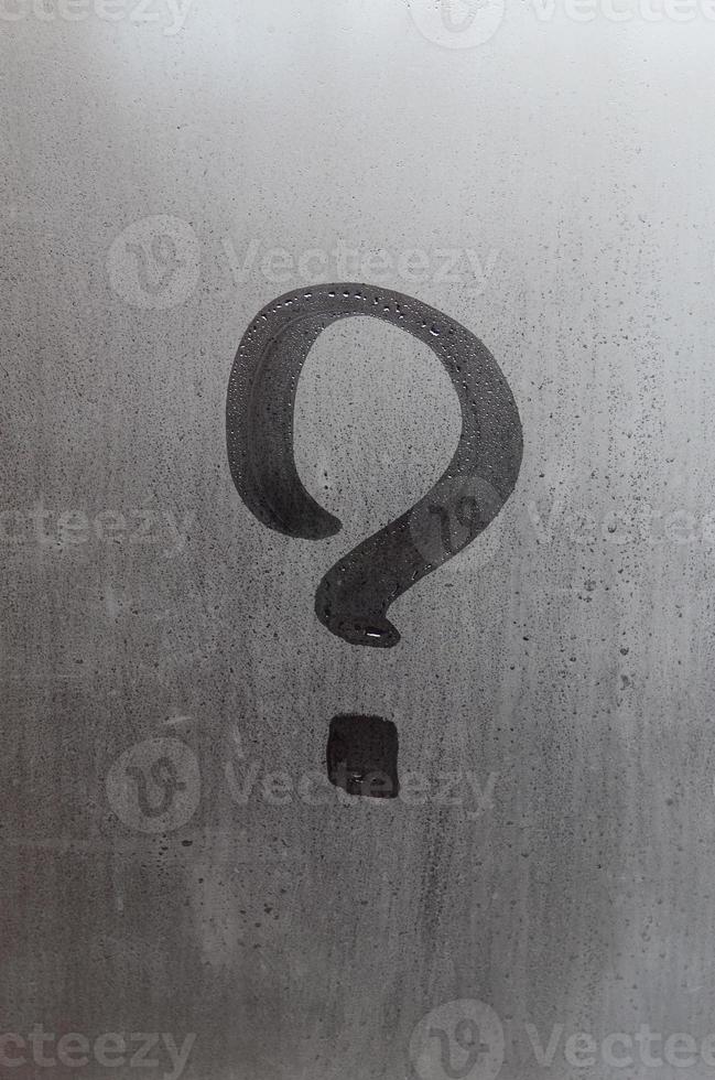 The inscription on glass, question mark concept. Question sign is painted on the surface of misted and wet window photo
