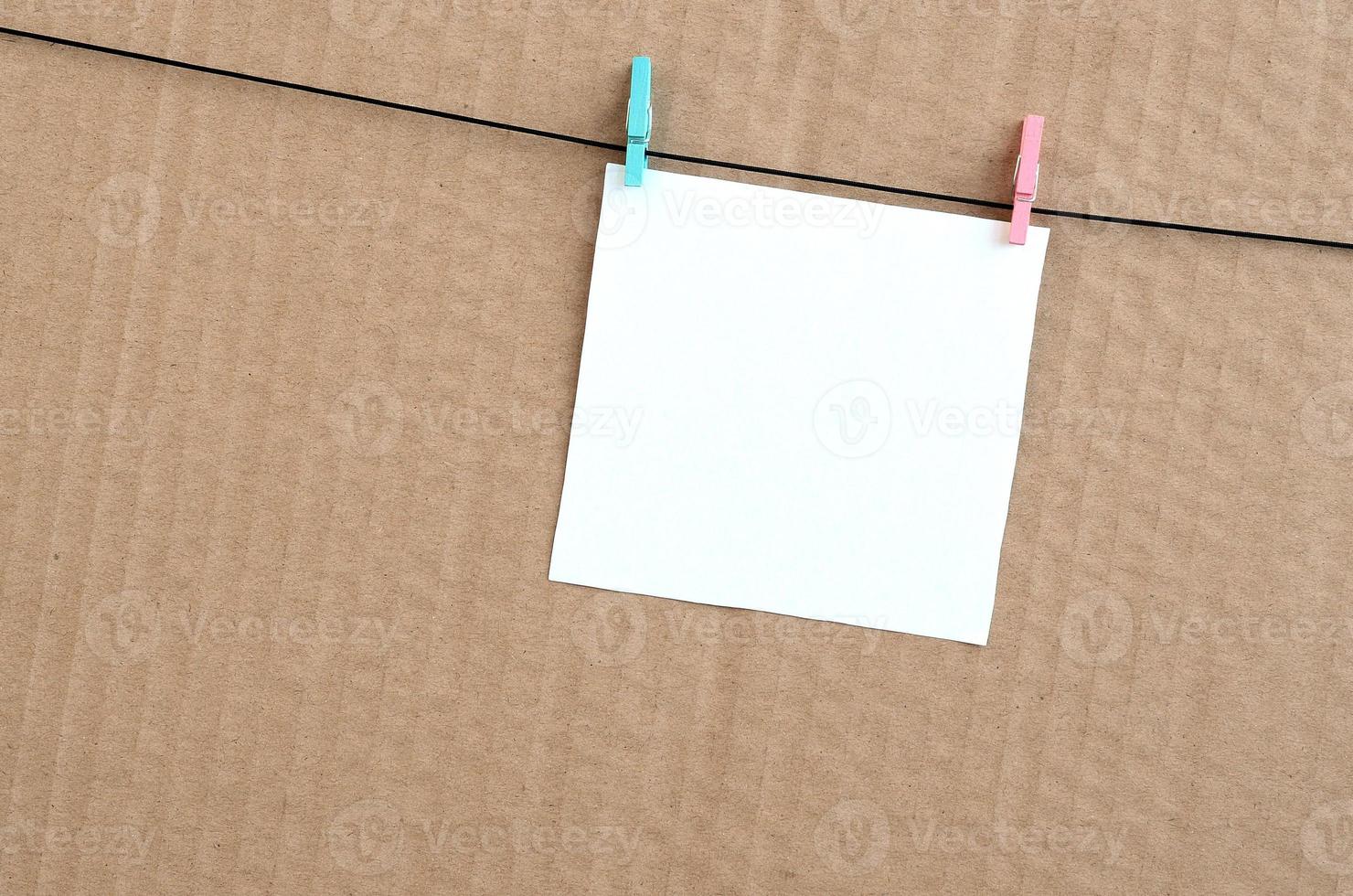 White blank card on rope on a brown cardboard background. Creative reminder, small sheet of paper on wooden clothespin, memo backdrop photo