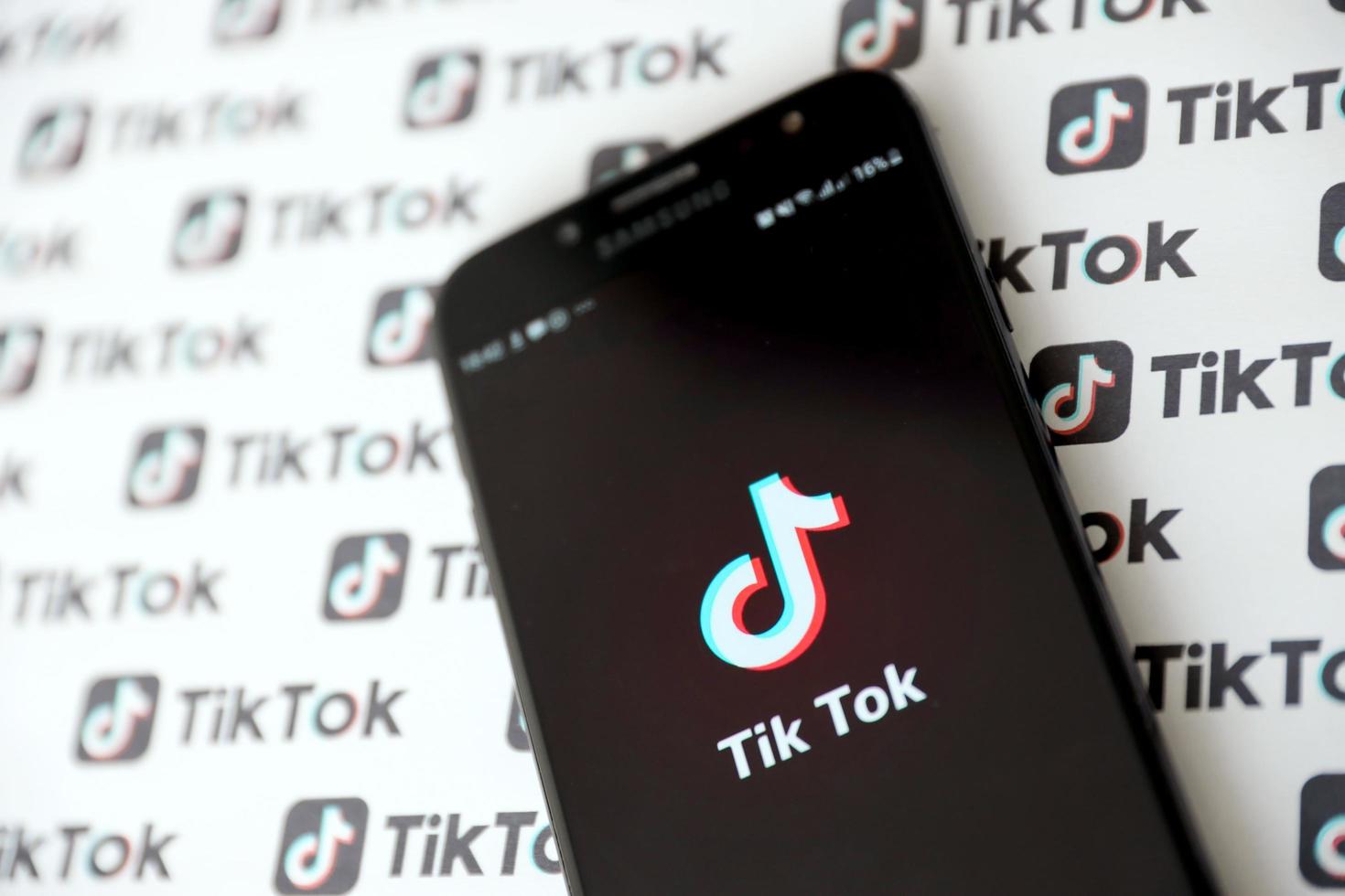 TERNOPIL, UKRAINE - MAY 2, 2022 Tik Tok smartphone app on screen and Many TikTok logo printed on paper. Tiktok or Douyin is a famous Chinese short-form video hosting service owned by ByteDance photo