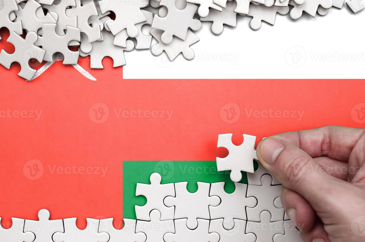 Oman flag  is depicted on a table on which the human hand folds a puzzle of white color photo