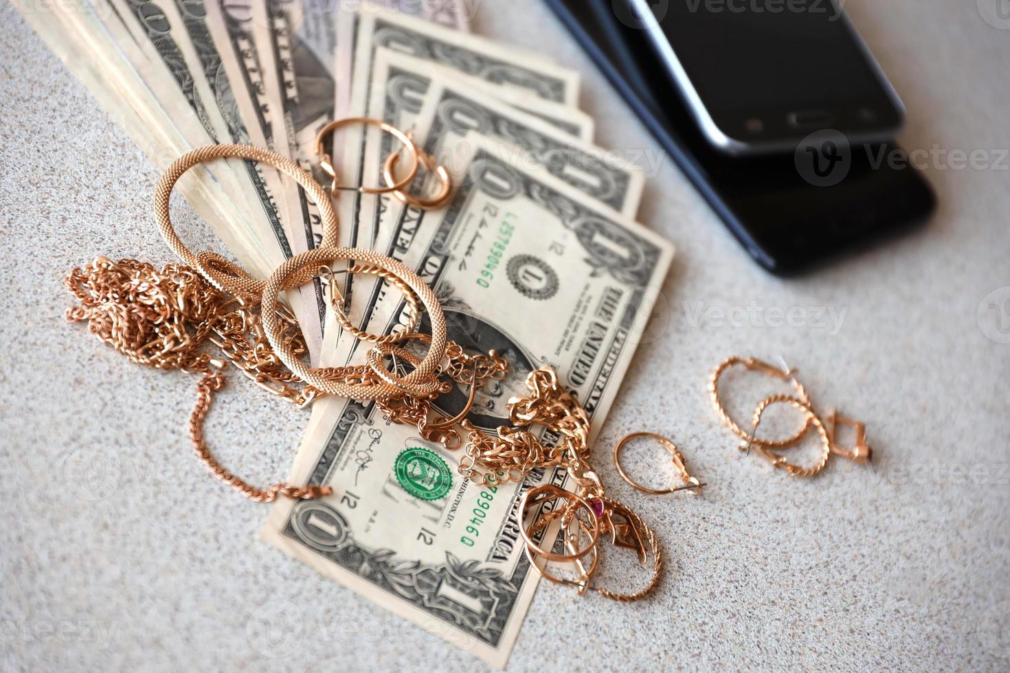 Many expensive golden jewerly rings, earrings and necklaces with big amount of US dollar bills close to smartphones. Pawn shop photo