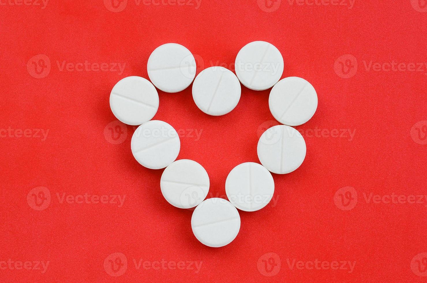 Several white tablets lie on a bright red background in the shape of a heart. Background image on medicine and pharmaceutical topics photo