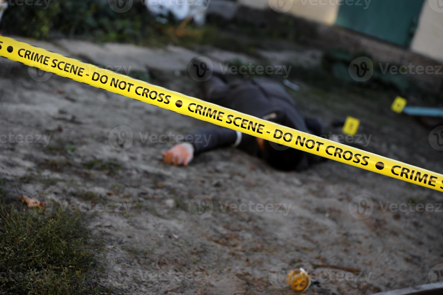 Victim of a violent crime in a backyard of residental house in evening. Dead man body under the yellow police line tape and evidence markers on crime scene photo