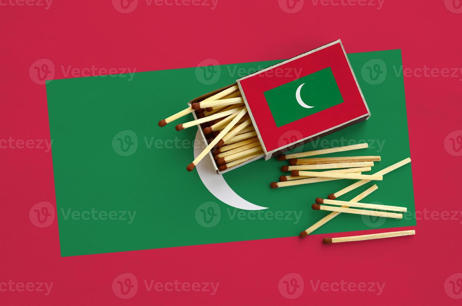 Maldives flag  is shown on an open matchbox, from which several matches fall and lies on a large flag photo