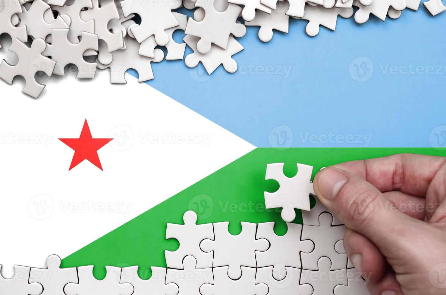 Djibouti flag  is depicted on a table on which the human hand folds a puzzle of white color photo