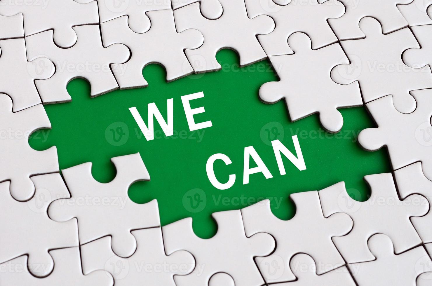White jigsaw puzzle in assembled state with missing elements forming a green space with white inscription. We can photo