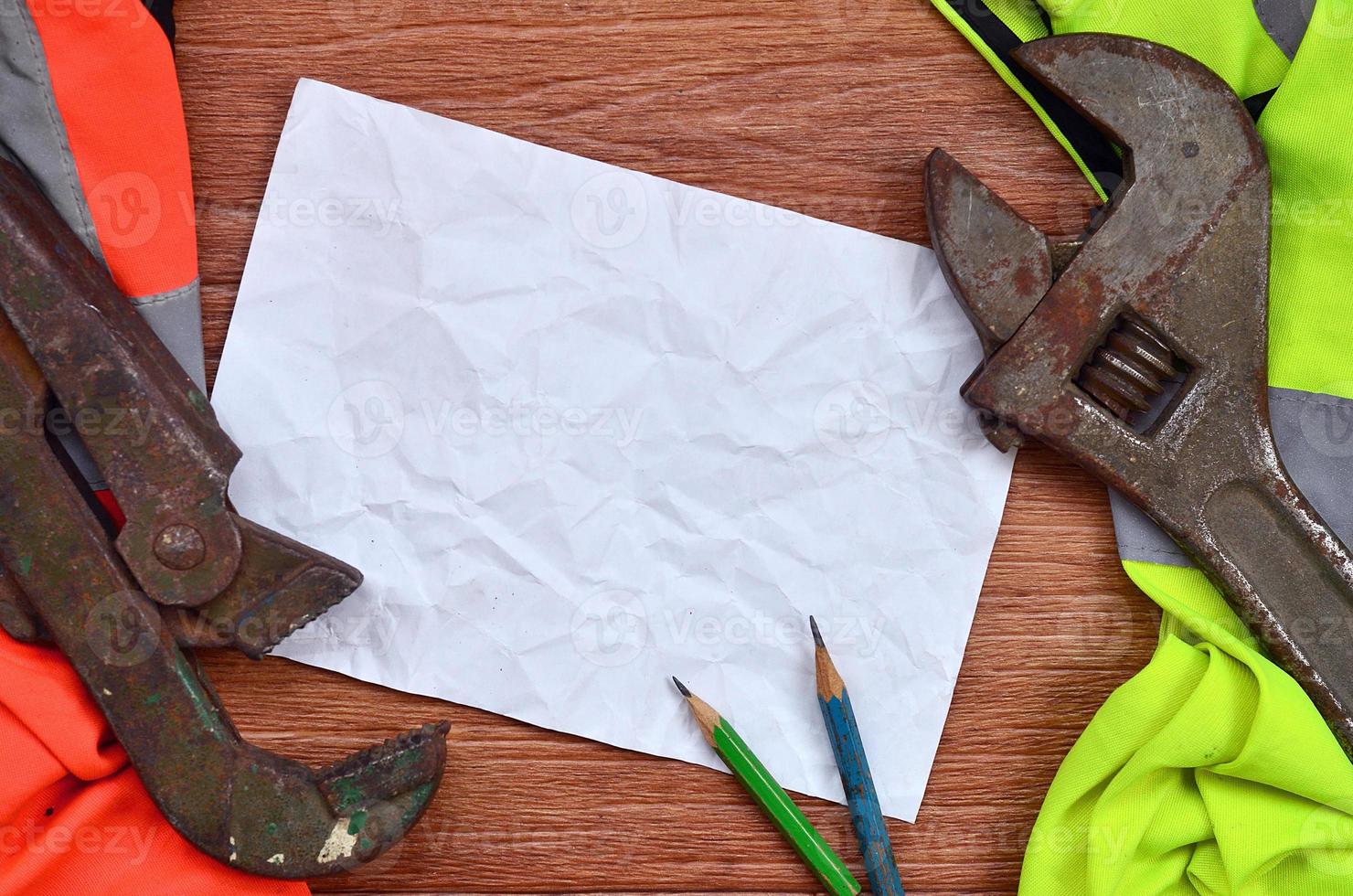 A crumpled sheet of paper with two pencils surrounded by green and orange working uniforms and adjustable wrenches photo