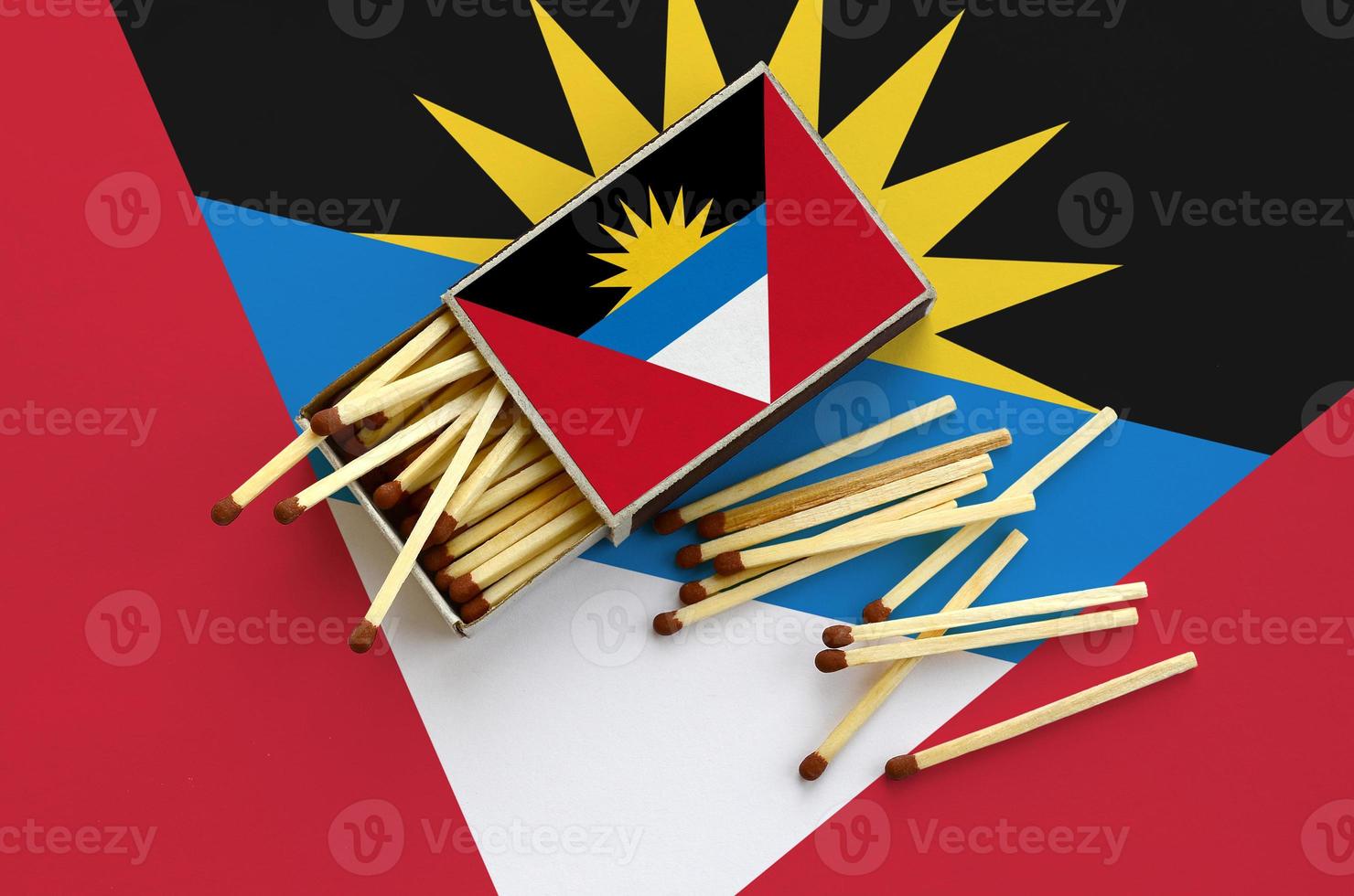 Antigua and Barbuda flag  is shown on an open matchbox, from which several matches fall and lies on a large flag photo