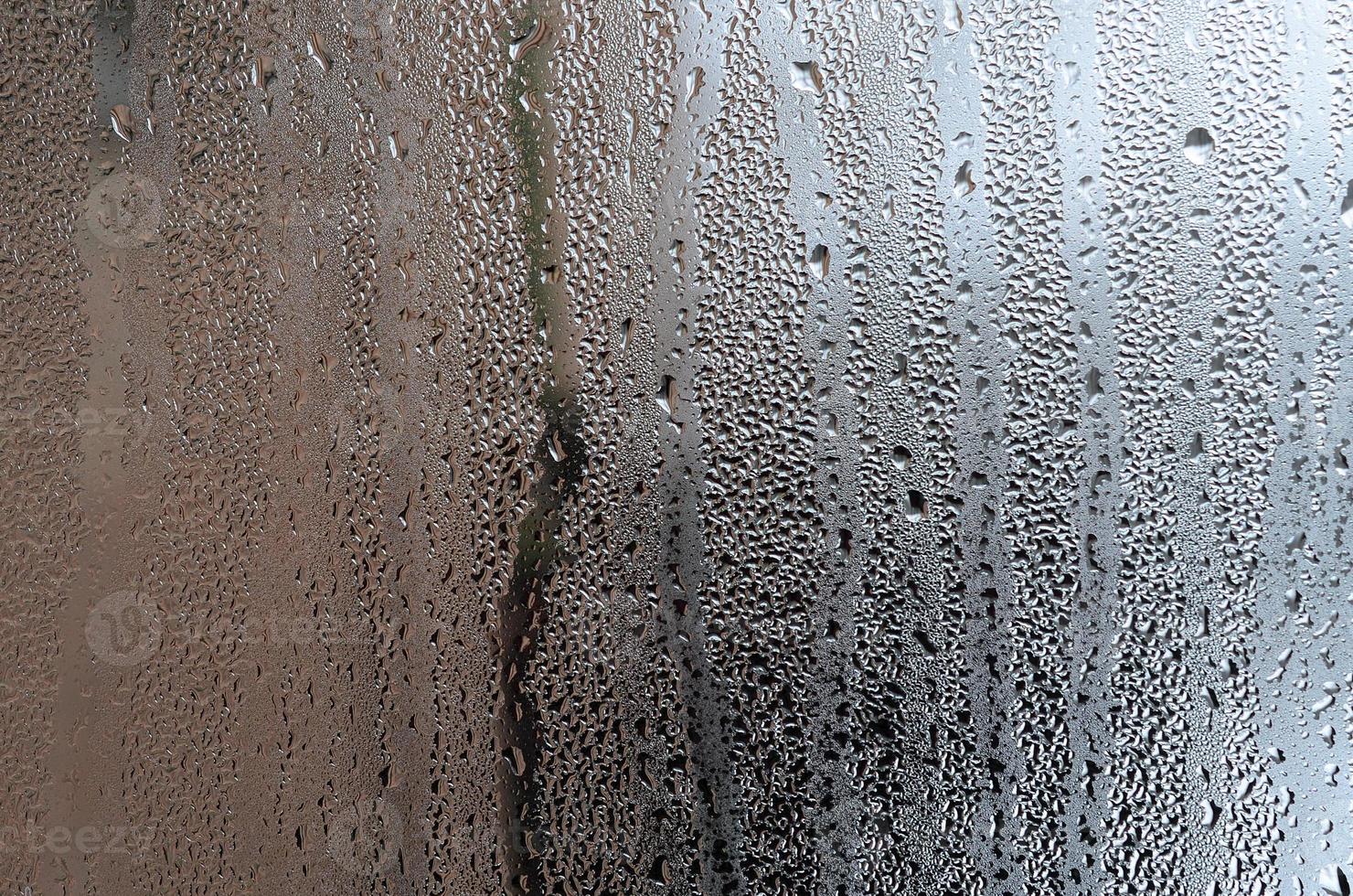 textura de una gota de lluvia sobre un fondo transparente húmedo de vidrio. tonificado en color gris foto