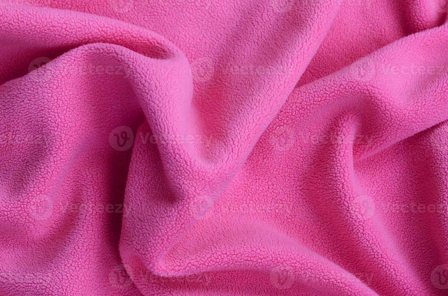 The blanket of furry pink fleece fabric. A background of light pink soft plush fleece material with a lot of relief folds photo