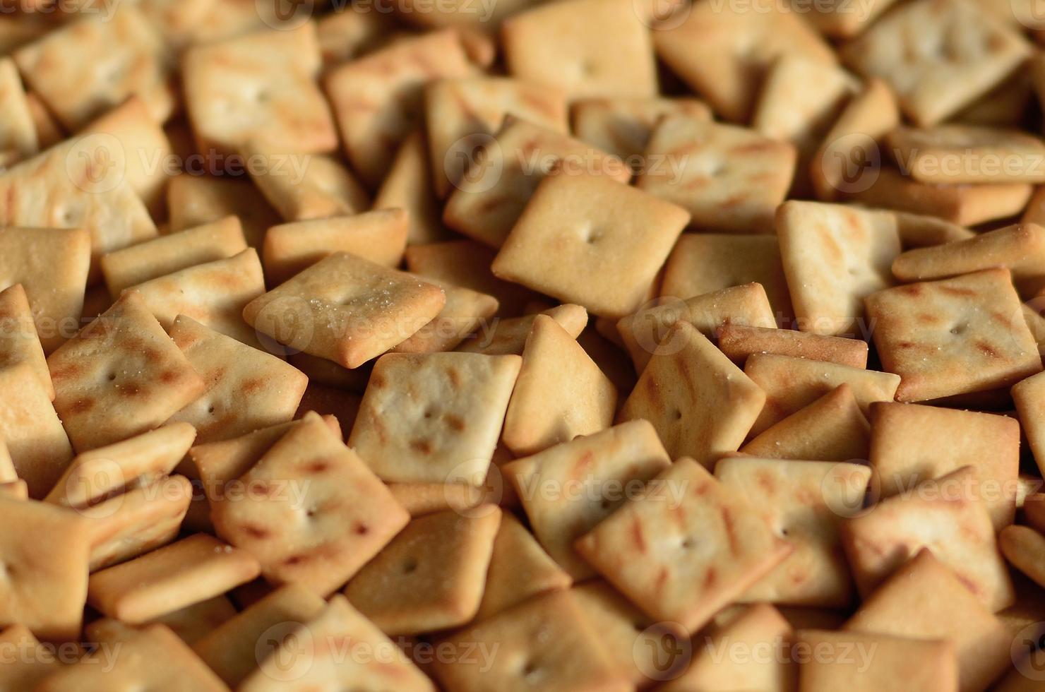 A lot of small cookies are square shaped. A pattern of a yellow salt cracker. Background image with salted pastry photo