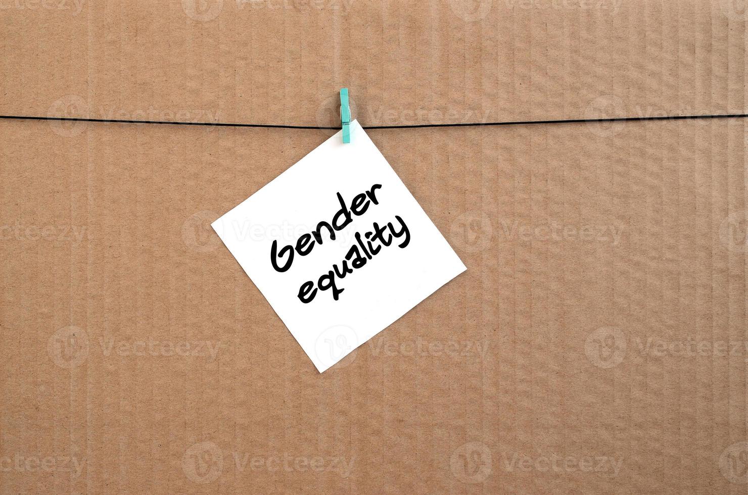 Gender equality. Note is written on a white sticker that hangs with a clothespin on a rope on a background of brown cardboard photo