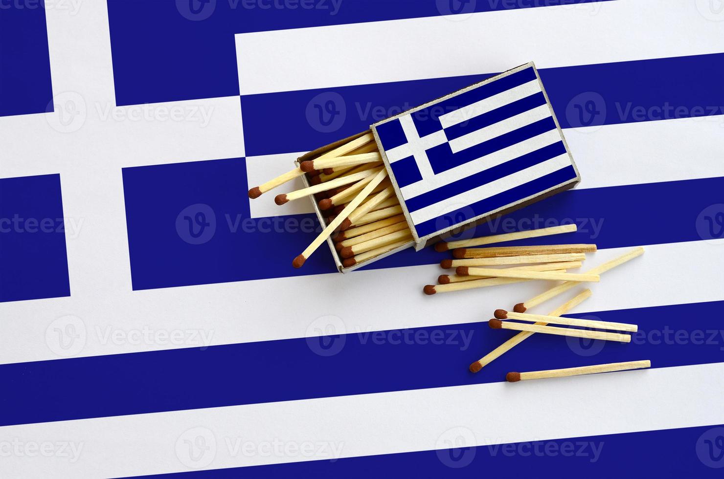 Greece flag  is shown on an open matchbox, from which several matches fall and lies on a large flag photo
