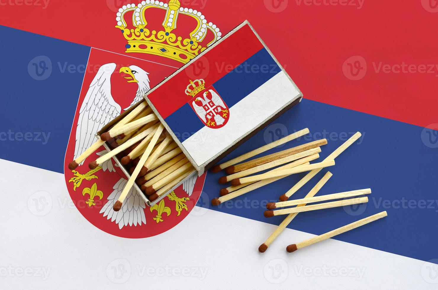 Serbia flag  is shown on an open matchbox, from which several matches fall and lies on a large flag photo