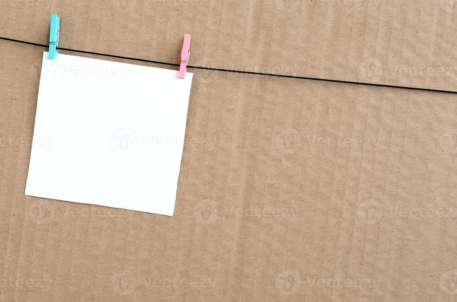 White blank card on rope on a brown cardboard background. Creative reminder, small sheet of paper on wooden clothespin, memo backdrop photo