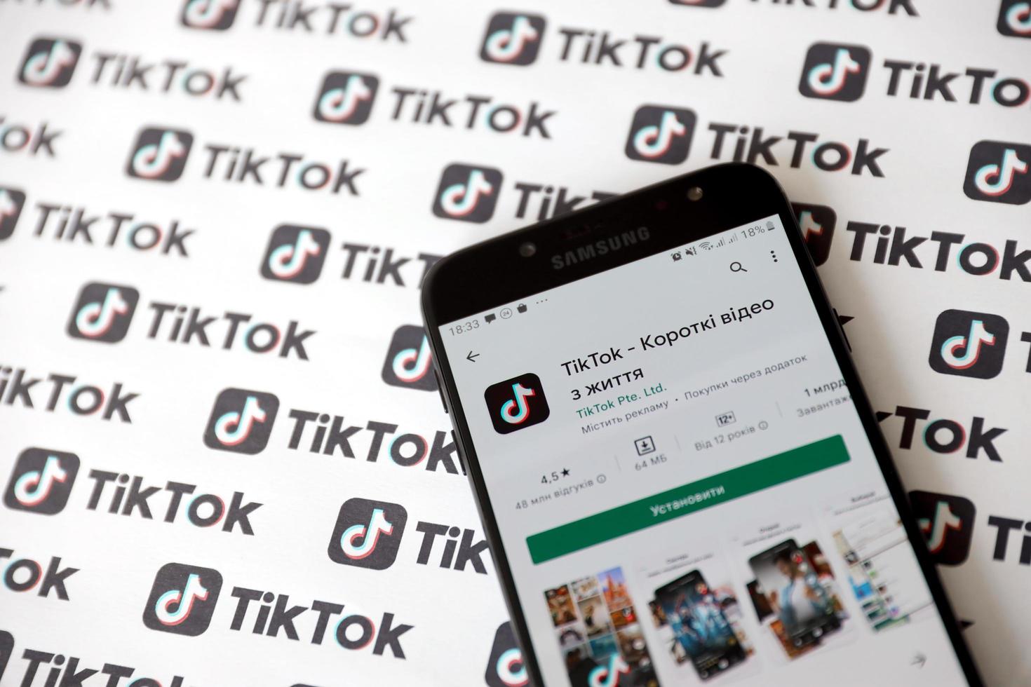 TERNOPIL, UKRAINE - MAY 2, 2022 Tik Tok smartphone app on screen and Many TikTok logo printed on paper. Tiktok or Douyin is a famous Chinese short-form video hosting service owned by ByteDance photo